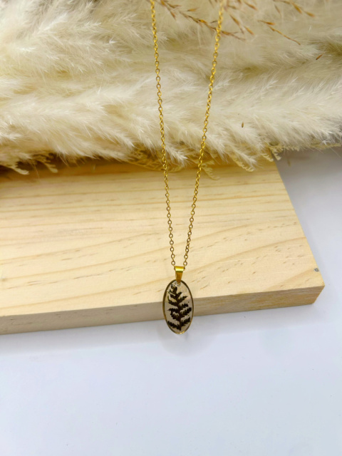 Naszyjnik handmade – owalna zawieszka z żywicy z zatopioną zieloną paprotką leśną na subtelnym pozłacanym łańcuszku, na naturalnym, drewnianym tle. Naszyjnik handmade – owalna zawieszka z żywicy z zatopioną zieloną paprotką leśną na subtelnym pozłacanym łańcuszku, na naturalnym, drewnianym tle.